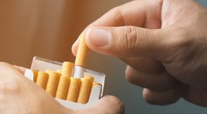 A hand pulling a cigarette from a packet