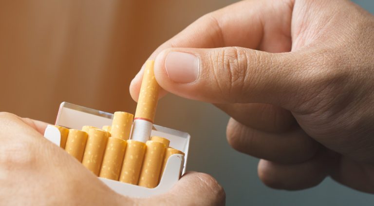 A hand pulling a cigarette from a packet