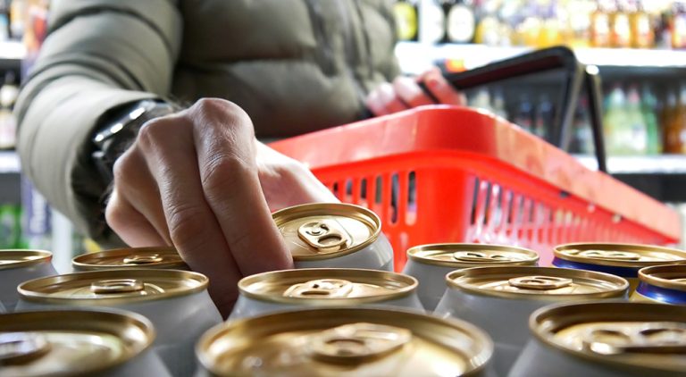 Person picking up a can of mid-strength beer in a shop while holding a shoppins basket