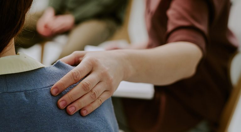 A person's hand on another person's shoulder, indicating a supportive environment